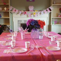 Two tables with a pink tablecloth decorated for a birthday.