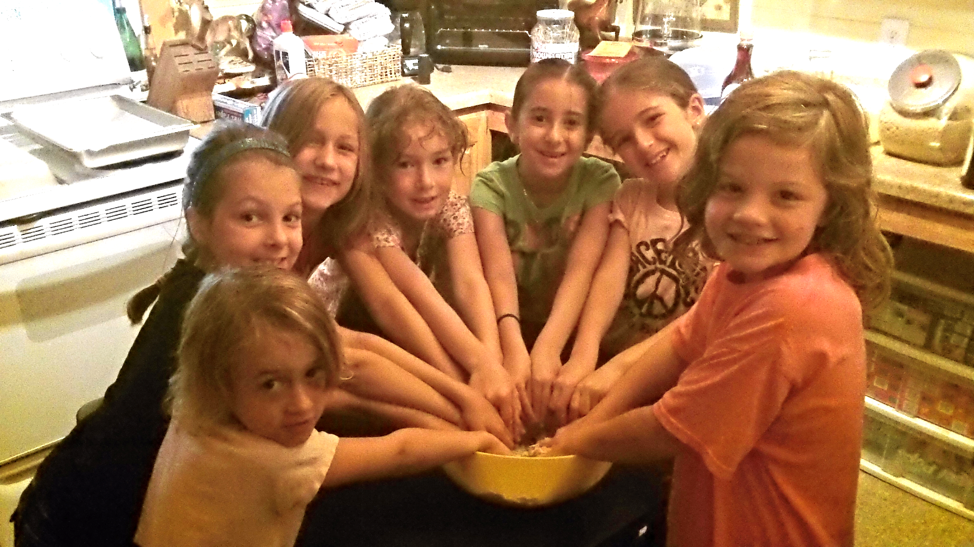 Seven children with their hands in a bowl.