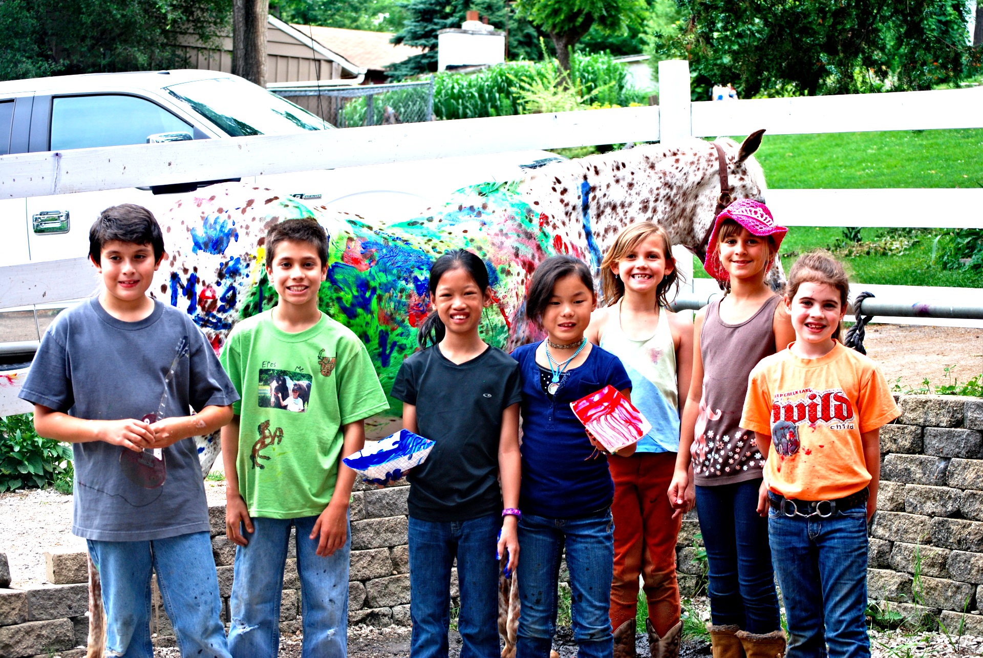7 kids standing in front of a painted horse.