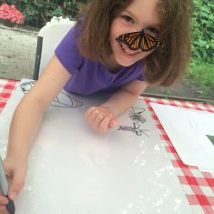 A young girl coloring with a butterfly on her face.